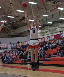 A thin young man jumps in the air and shoots a basketball.